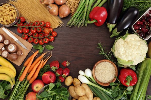 Overhead view of a dark wooden table covered with a colorful variety of fresh fruits, vegetables, herbs, and pasta.