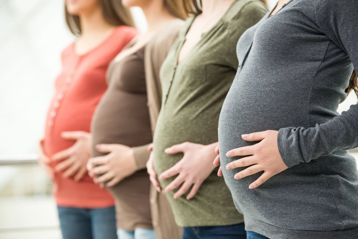 Four pregnant women standing in a row, with their hands resting on their abdomens.
