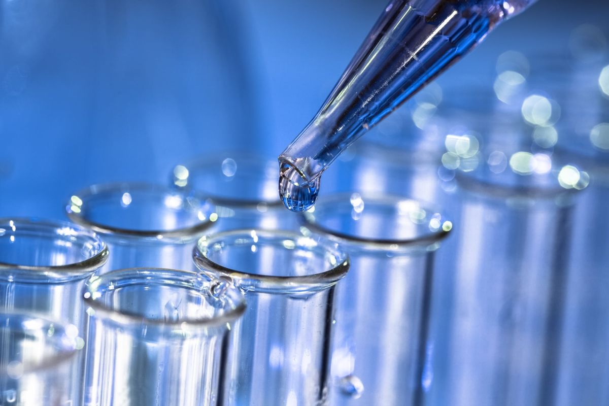 Close-up of a pipette dripping chemicals into a row of glass test tubes.